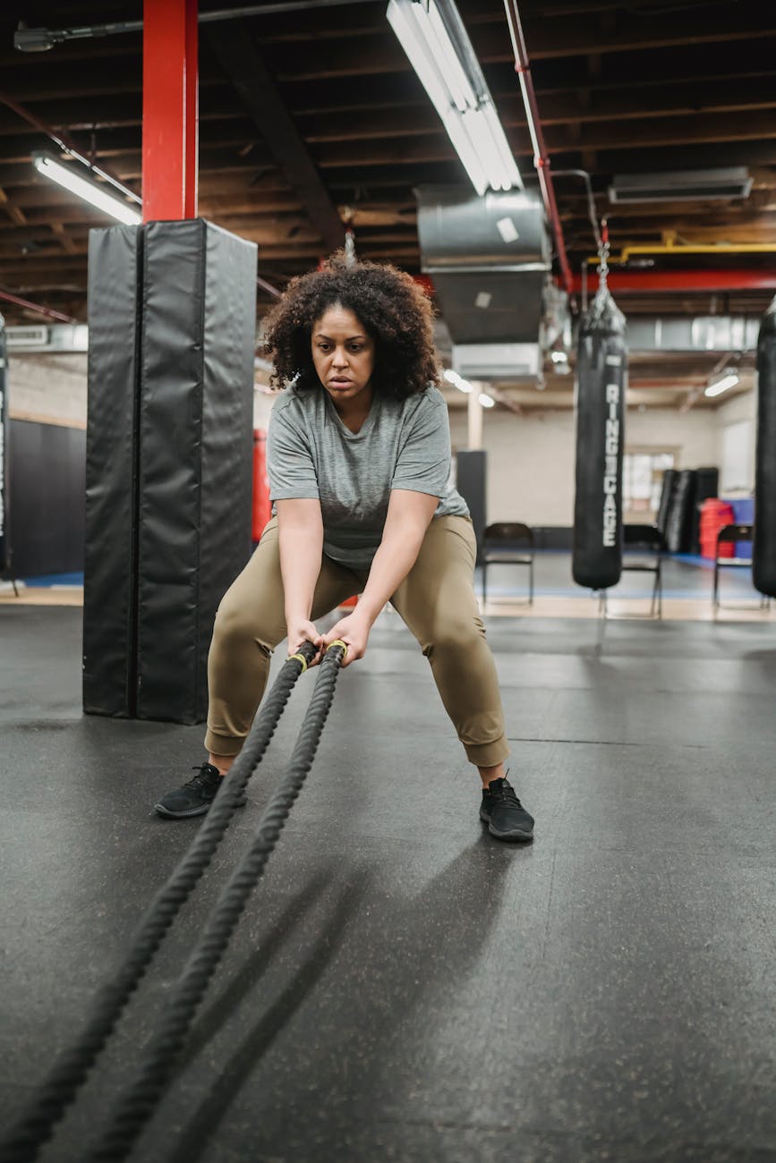 energetic plump woman exercising with battle ropes in gym